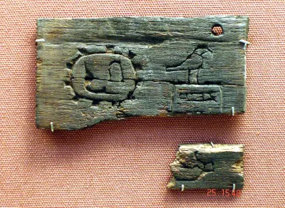 Two fragments of a 1st Dynasty ebony label, each bearing incised markings. The larger records the name of Narmer alongside a place name. Bri